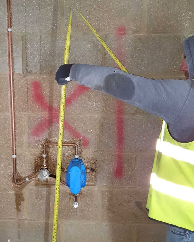 An installer measuring pipe positions on an unfinished wall
